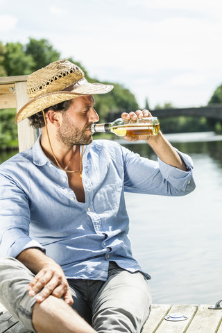 Mann sitzt auf einer Plattform am Wasser und trinkt Bier, lizenzfreies Stockfoto