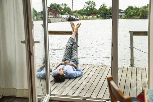 Mann liegt auf dem Holzdeck eines Hausbootes - FMKF001973