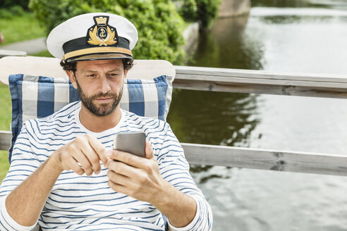 Man wearing captain's hat looking at cell phone - FMKF001990