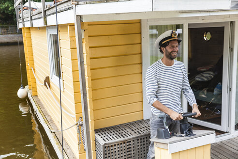 Man wearing captain's hat having a trip on a house boat - FMKF001986