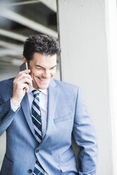 Portrait of smiling businessman telephoning with smartphone - UUF005346