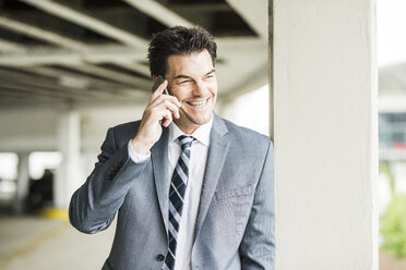 Porträt eines lächelnden Geschäftsmannes, der mit einem Smartphone telefoniert - UUF005349