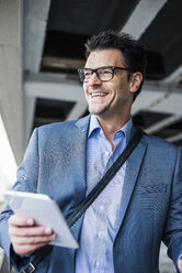 Portrait of smiling businessman with mini tablet - UUF005351