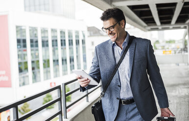 Happy businessman on business trip looking at his mini tablet - UUF005353