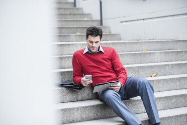 Geschäftsmann mit digitalem Tablet und Smartphone auf einer Treppe sitzend - UUF005376