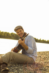 Porträt eines glücklichen Mannes, der am Abend am Flussufer Gitarre spielt - UUF005385