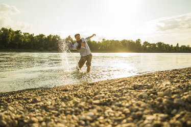 Mann steht am Flussufer und spritzt mit Wasser - UUF005390