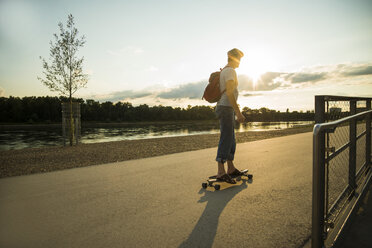 Mann auf Skateboard in der Abenddämmerung stehend - UUF005405