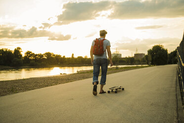 Back view of man with backpack and skateboard in the evening twilight - UUF005401