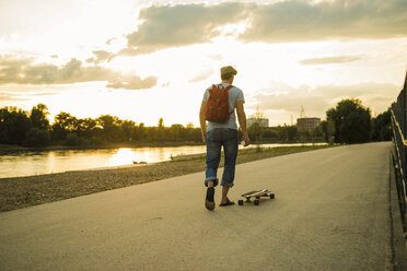 Rückenansicht eines Mannes mit Rucksack und Skateboard in der Abenddämmerung - UUF005401