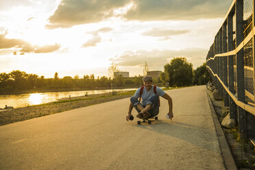 Man sitting on skateboard in the evening twilight - UUF005402