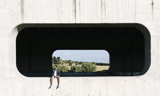 Spain, Tarragona, young man sitting in niche of a concrete wall - JRFF000007
