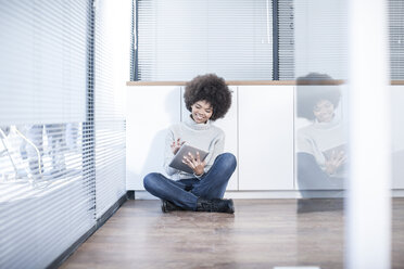 Woman sitting on the floor in office using digital tablet - ZEF007213