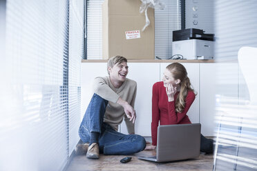 Two colleagues sitting on office floor using laptop - ZEF007216