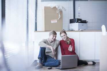 Two colleagues sitting on office floor using laptop - ZEF007217