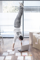 Man doing a handstand at laptop next to cardboard boxes - ZEF007220