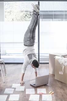 Mann macht einen Handstand am Laptop neben Kartons - ZEF007220