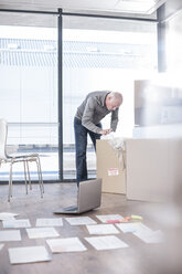 Mann in neuem Büro packt Karton aus - ZEF007221