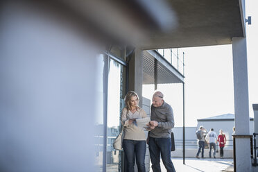 Two colleagues outside office building discussing paper - ZEF007229