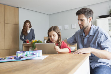 Kleines Mädchen und ihr Vater sitzen am Küchentisch und schauen auf ein digitales Tablet - RBF003371