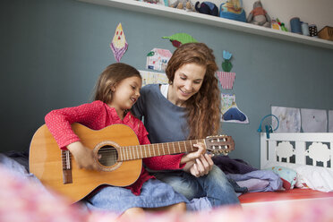 Little girl playing guitar while her mother listening - RBF003385