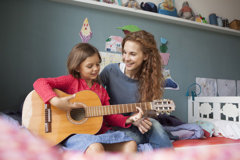Little girl playing guitar while her mother listening stock photo
