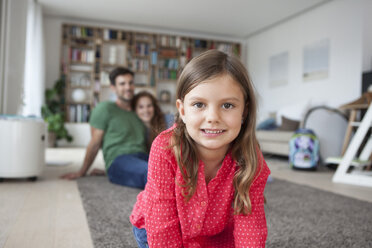 Portrait of smiling little girl and her parents in the background in the living room - RBF003390