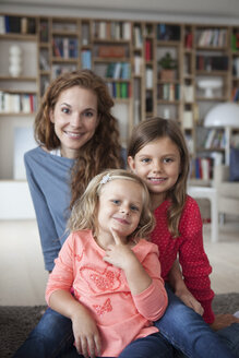 Porträt von zwei kleinen Schwestern und ihrer Mutter im Hintergrund, die auf dem Boden im Wohnzimmer sitzen - RBF003391
