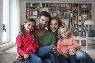 Family portrait of couple with two little girls sitting on the floor of living room - RBF003392