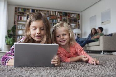 Porträt von zwei kleinen Schwestern auf dem Boden liegend im Wohnzimmer mit digitalem Tablet - RBF003396