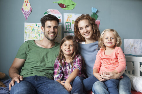 Familienbild eines Paares mit ihren kleinen Töchtern, die zusammen auf dem Bett im Kinderzimmer sitzen - RBF003403