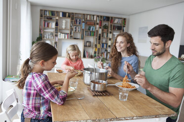 Little girl sitting at dining table with her parents and sister eating spaghetti - RBF003413