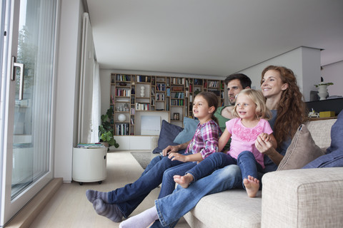 Couple and two little girls sitting on couch in the living room looking through terrace door stock photo