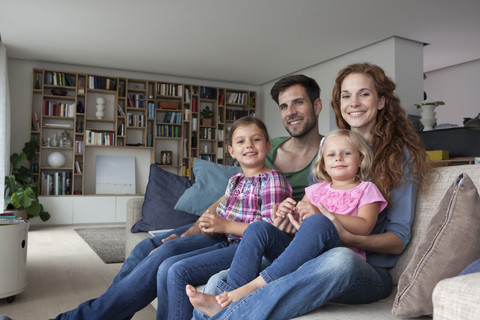 Family portrait of couple with two little girls sitting together on couch in the living room stock photo