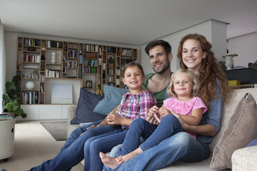 Family portrait of couple with two little girls sitting together on couch in the living room - RBF003416