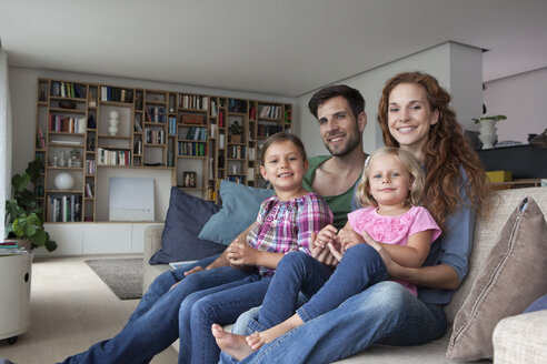Familienporträt eines Paares mit zwei kleinen Mädchen, die zusammen auf der Couch im Wohnzimmer sitzen - RBF003416