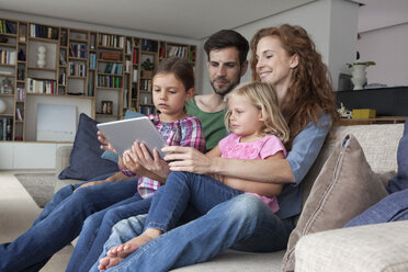 Ehepaar sitzt mit seinen zwei kleinen Töchtern auf der Couch im Wohnzimmer und schaut auf ein digitales Tablet - RBF003417