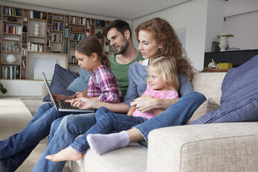 Ehepaar sitzt mit ihren beiden kleinen Töchtern auf der Couch im Wohnzimmer und schaut auf den Laptop - RBF003418
