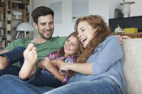 Glückliches Paar und kleine Tochter auf der Couch zu Hause - RBF003424