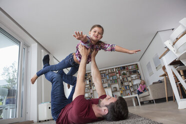 Man lying on the floor at living room playing with his little daughter - RBF003425