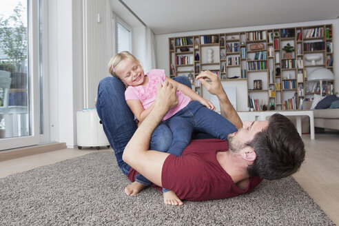 Mann liegt auf dem Boden im Wohnzimmer und spielt mit seiner kleinen Tochter - RBF003426
