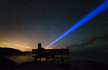 Spain, Ortigueira, Loiba, silhouette of a man sitting on bench under starry sky with blue ray - RAEF000355