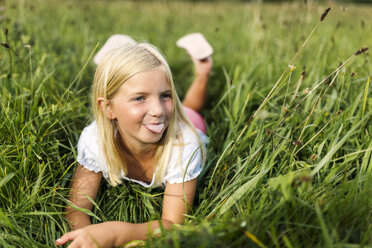 Portrait of girl lying on a meadow sticking out tongue - MGOF000505