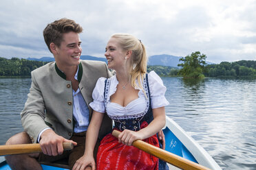 Germany, Bavaria, happy young couple wearing traditional clothes sitting in a rowing boat on Staffelsee - TCF004860