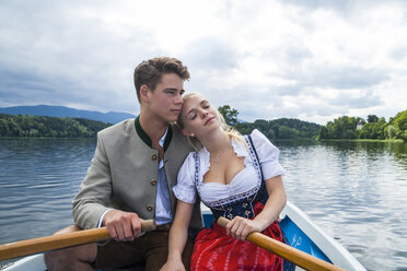 Germany, Bavaria, young couple in love wearing traditional clothes sitting in a rowing boat on Staffelsee - TCF004861