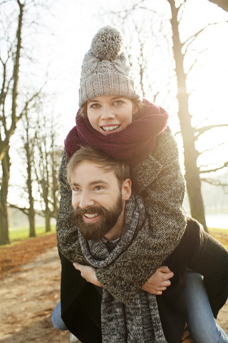 Junger Mann trägt Freundin im Herbst huckepack, lizenzfreies Stockfoto