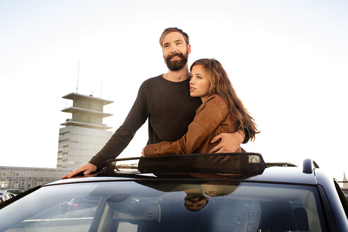Glückliches Paar schaut durch das Schiebedach eines Autos und umarmt sich - PESF000163