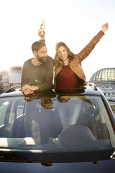 Happy couple with beer bottle looking through sunroof of a car - PESF000164