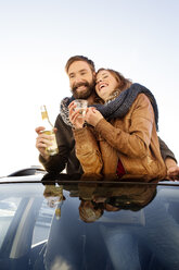 Happy couple looking through sunroof of a car sharing a scarf - PESF000178