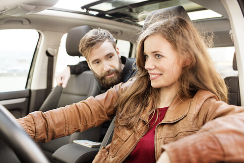 Lächelnde junge Frau am Steuer eines Autos mit einem Mann auf dem Rücksitz - PESF000174